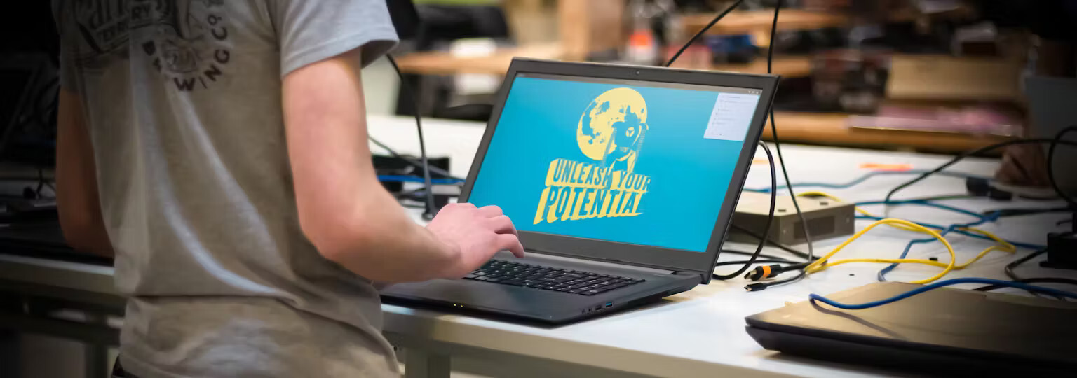 Picture of a technician testing a laptop on a workbench. The workbench includes other laptops, switches, and cables.